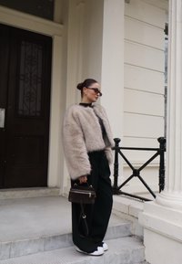 Ψεύτικο γούνινο μπουφάν σε ανοιχτό μπεζ χρώμα, υπερμεγέθες εφαρμογή; μαύρη μπλούζα, παντελόνι σε φαρδιά γραμμή; καφέ τσάντα; μαύρα γυαλιά ηλίου; �έξω κοντά σε ένα κτίριο.