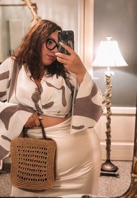 Blusa a righe con texture e maniche a campana; gonna bianca; borsa in tessuto marrone a forma quadrata con motivo aperto; specchio sullo sfondo.
