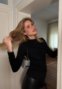 Μαύρο μακρυμάνικο τοπ με ραφές, συνδυασμένο με λαμπερά μαύρα κολάν. Μια μικρή, ασημένια τσάντα με studs φοριέται διαγώνια στον ώμο.