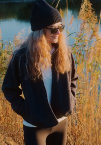 Tamsiai mėlynos spalvos vilnos striukė su laisvu siluetu, derinama su balta palaidine ir juodomis tamprėmis. Aksesuarai: juoda kepurė ir saulės akiniai.