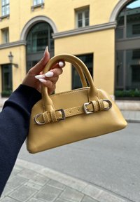 Gul läderhandväska med två korta handtag, silverfärgade detaljer och en blank finish. Kompakt design med synliga stygn.
