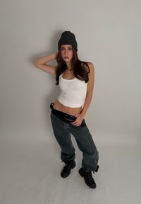 Débardeur blanc à côtes, ceinture en cuir synthétique noir, jean oversize en denim foncé, bottes noires à lacets et bonnet en tricot foncé.