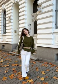 Oliwkowozielony, oversize'owy sweter, białe rozkloszowane spodnie, wzorzysty torebka, skórzany pasek, spacer po bruku z rozsypanymi liśćmi jesiennymi.
