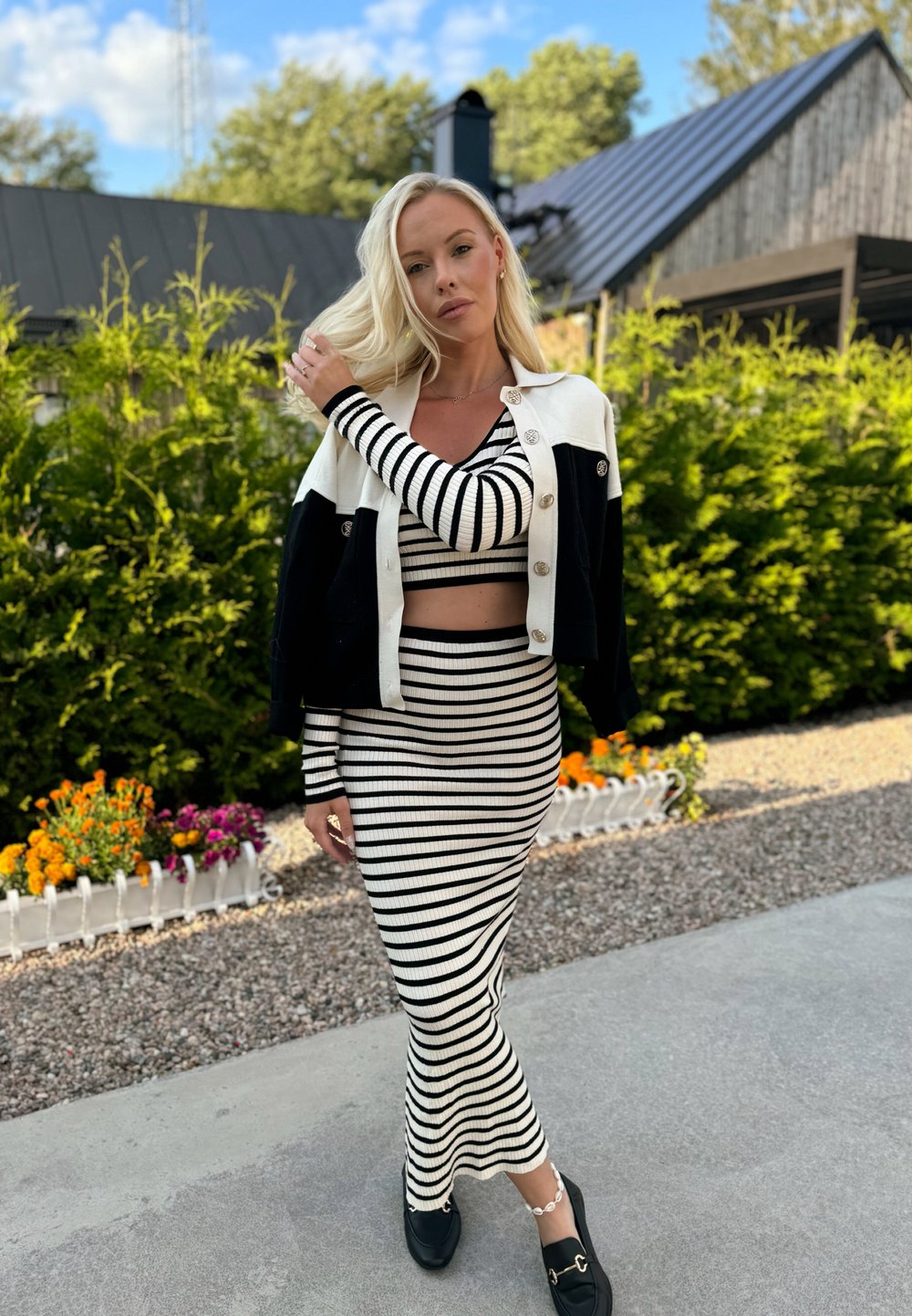 Δίχρωμο σε μαύρο και άσπρο πλεκτό σετ δύο κομματιών με cropped τοπ και μακριά φούστα, συνδυασμένο με μια ζακέτα σε μαύρο και κρεμ χρώμα.