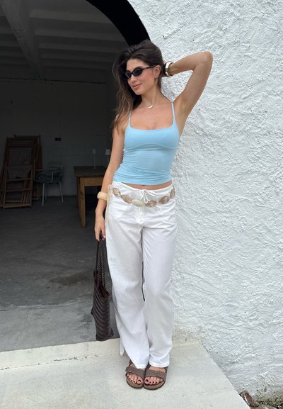 Top de tirantes ajustado azul claro combinado con pantalones anchos blancos de cintura alta. Un cinturón beige grueso y sandalias marrones completan el look.