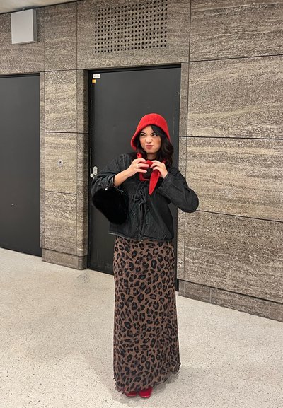 Chaqueta negra corta con capucha de punto roja, bufanda roja y falda larga con estampado de leopardo. El conjunto se completa con zapatos rojos y un bolso de piel negro.
