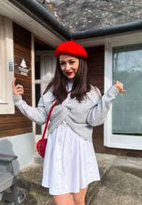 Grå stickad tröja knuten fram, vit skjortklänning och en röd basker. Minimala accessoarer, med en röd axelväska och neutral bakgrund.