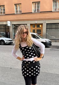 Črna in bela obleka s pikami, ki je preplastena z belo dolgimi rokavi, v kombinaciji z črno torbico s studenci in širokim črnim pasom.