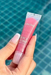 Lucidalabbra Juicy Tubes di Lancome in un tubo trasparente, riempito con un prodotto rosa iridescente. Presenta un coperchio a torsione e un branding minimal.