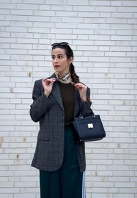 Grå rutete oversized blazer, mørkegrønn genser, svart håndveske med gullspenne, fargerik mønstret skjerf og mørkegrønne vide bukser.