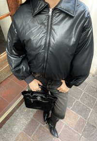 Giacca cropped nera in pelle con colletto, con maniche ampie, abbinata a una borsa nera e jeans in denim scuro. Gli stivali hanno la punta affusolata.