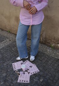 Lyserød stribet skjorte med knapper, blå jeans, hvide og grå sneakers. Lyserøde Vogue-magasiner og en lyserød kaffekop på brostensjorden.