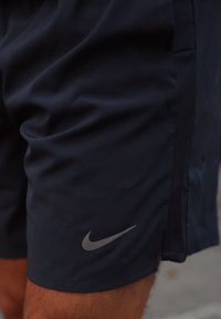 Shorts de sport bleu marine en tissu lisse ; présentent un panneau latéral en mesh subtil et un logo Nike gris sur la partie inférieure de la jambe gauche.