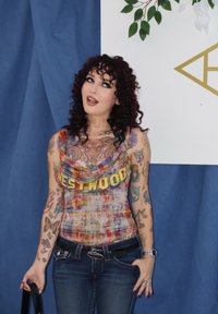 Erinevate värvidega ilma varrukateta tops, millel on kergelt laskuv kaelus ja millel on kiri "WESTWOOD". Ühendatud tumedate siniste slim-fit teksadega ja mitmete tätoveeringutega.