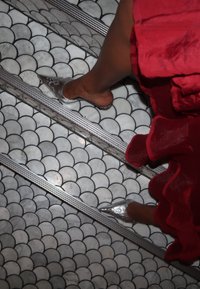 Femme portant des escarpins argentés à bouts pointus et une robe rouge à volants, marchant sur des escaliers carrelés à motifs avec des bords en métal.