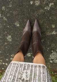 Bottes courtes en cuir marron avec un bout pointu, dotées de fermetures éclair latérales et d'une texture lisse, portées au-dessus d'une jupe argentée à sequins.