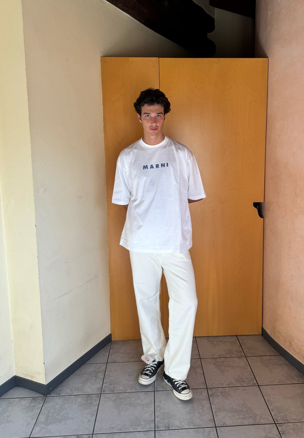 T-shirt oversized branca com o logótipo "MARNI", combinada com calças largas creme e ténis pretos. Tecido suave, ajuste casual, design minimalista.