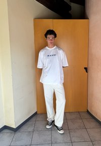 T-shirt oversized branca com o logótipo "MARNI", combinada com calças largas creme e ténis pretos. Tecido suave, ajuste casual, design minimalista.