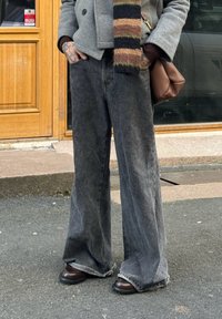Jean denim gris foncé à jambes larges avec une finition délavée. Associé à des chaussures en cuir marron et une veste grise. Accentué par une écharpe rayée multicolore.