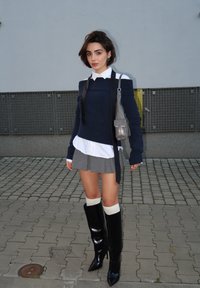 Ναυτικό φούτερ με ακάλυπτους ώμους τοποθετημένο πάνω από ένα λευκό μπλουζάκι, γκρίζα πλισέ φούστα και γυαλιστερές μαύρες μπότες μέχρι το γόνατο με κρέμ κάλτσες. Ασημένια τσάντα.