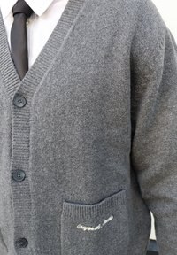 Cardigan en laine grise avec col en V, col côtelé, cinq boutons et une poche gauche ornée de texte brodé blanc.