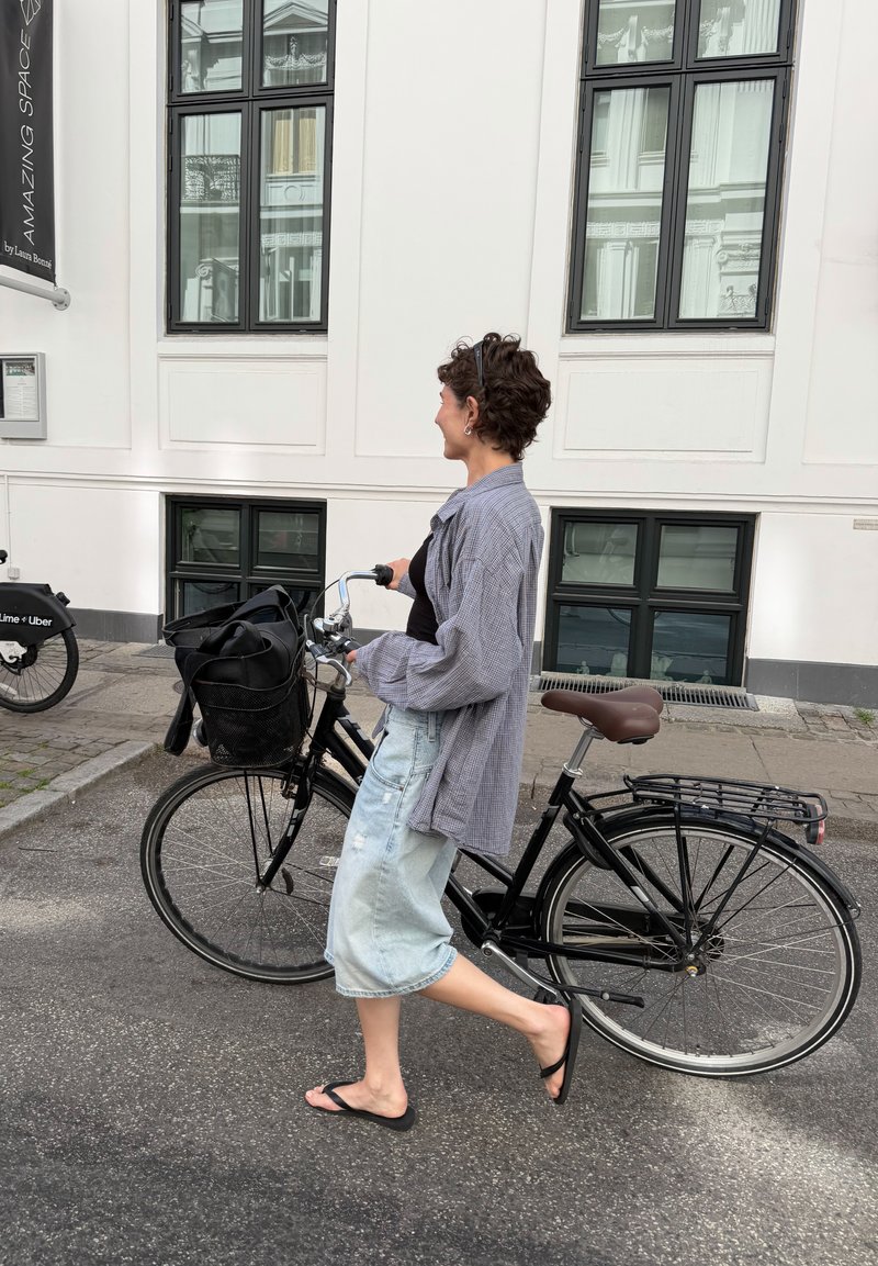 Personne marchant avec un vélo noir dans une rue urbaine à côté d'un bâtiment blanc avec de grandes fenêtres.