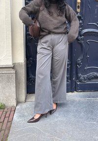 Sive visoke hlače širokih nogavic z discerniranim pinstripe vzorcem, v kompletu z rjavim pletenim puloverjem in rjavimi čevlji s koničastim sprednjim delom.