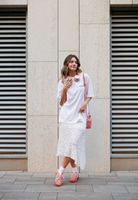 Λευκό oversized t-shirt, λευκή δαντελωτή midi φούστα, ροζ αθλητικά παπούτσια, ροζ τσάντα χιαστί και ροζ ακουστικά. Υφές και επίπεδες σχεδίες.