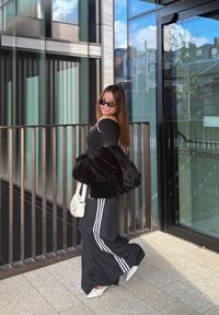 Sort faux fur jakke over en sort langærmet top, parret med sorte bukser med hvide striber, hvide hæle og en hvid crossbody taske.