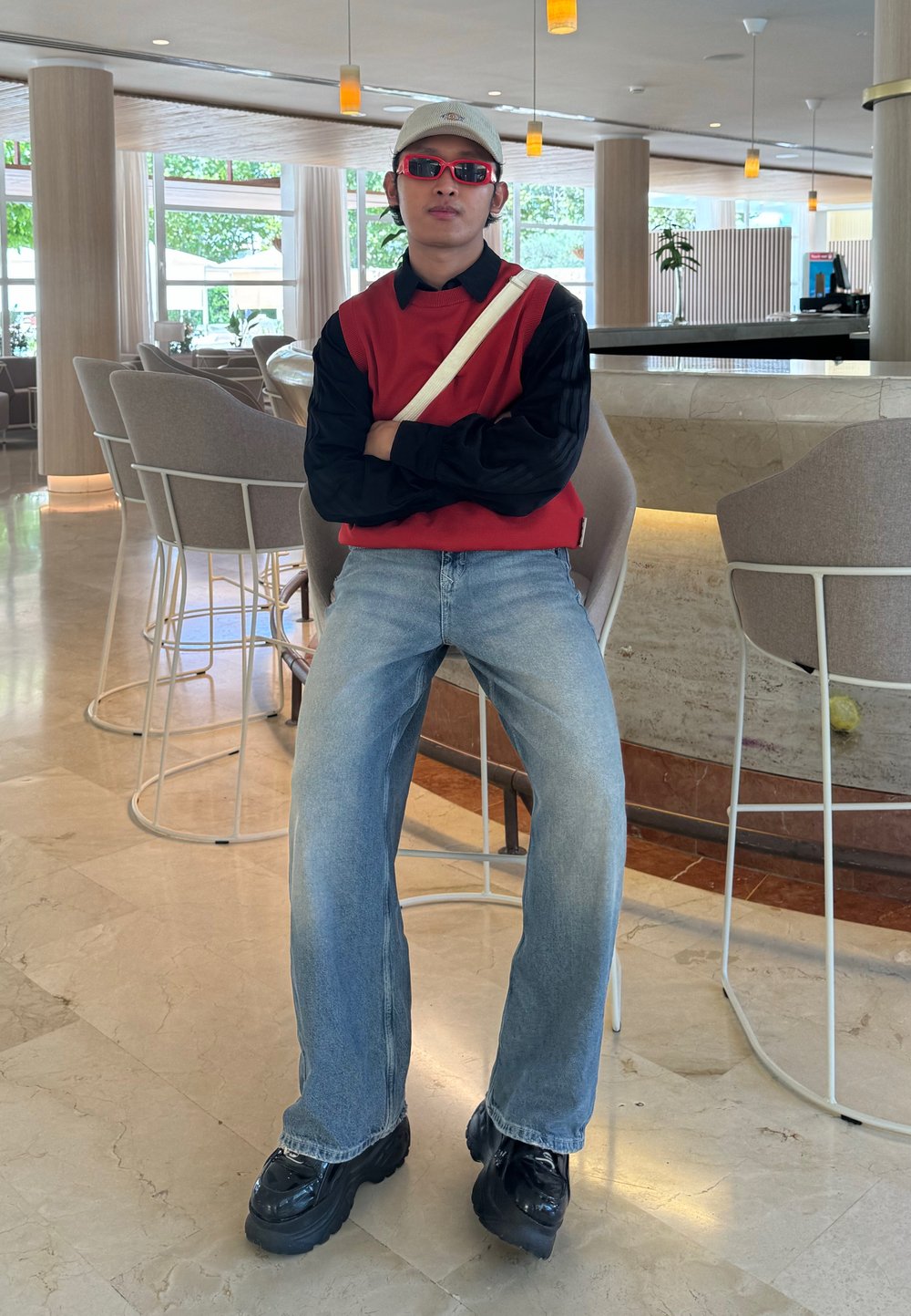 Rojo suéter sin mangas sobre una camiseta negra de manga larga, combinado con unos jeans baggy azul claro y zapatos chunky negros. Los accesorios incluyen una gorra de béisbol y gafas de sol rojas.