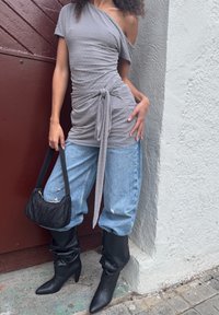 Sivi top s polkama koji otkriva ramena, zavezan u struku, upareno s lepršavim svijetloplavim trapericama i crnim čizmama do koljena. Mala crna torbica.