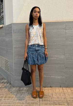 Top de tirantes con lentejuelas en rosa pálido, combinado con una falda de mezclilla con volantes. Un bolso negro y sandalias de plataforma marrones completan el conjunto.