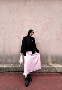 Μαύρο μπουφάν με επένδυση φλις πάνω από μαύρο τοπ, ελαφρώς ροζ σατέν φούστα, χοντρές μαύρες πλατφόρμες, ροζ τσάντα με χρυσά αξεσουάρ.