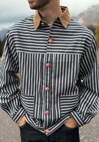 Randig jacka i marinblått och vitt med krage i beige, med röda knappar och två framfickor, tillverkad av texturerat tyg.