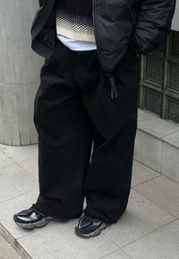 Sorte vide bukser i denim, med løs passform og glatt tekstur. Kombinert med svarte og grå atletiske sko.