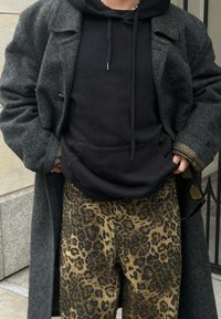 Siv šalski plašč, črna kapuca in rjave hlače z leopardjim vzorcem. Oblačilo se ponaša z teksturirano tkanino in kontrastnimi barvami.