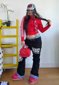 Piros cipzáros dzseki fehér csíkokkal, fekete nadrág "HASE2" felirattal, piros kézitáska és piros cipő. Kiegészítők között szerepel egy kockás nyakkendő és sapka.
