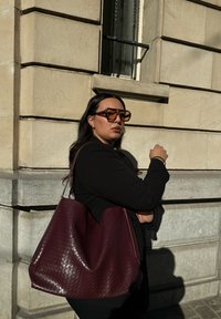 Sac fourre-tout en cuir tissé bordeaux avec une forme décontractée. Il dispose de fines bretelles et d'une surface texturée.