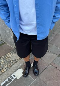 Camisa azul claro con botones, camiseta blanca debajo, pantalones cortos negros, calcetas negras y zapatos negros pulidos. Texturas planas y suaves.