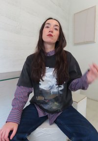 Sort t-shirt med landskabsprint iført over en blå og rød stribet skjorte med krave; kombineret med mørkeblå jeans. Neutralfarvet baggrund.