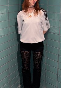 Valge lühikeste varrukatega Adidas särk, mustade lillemustriliste pitsleggingsidega. Taustaks on türkiissinine plaaditud sein.