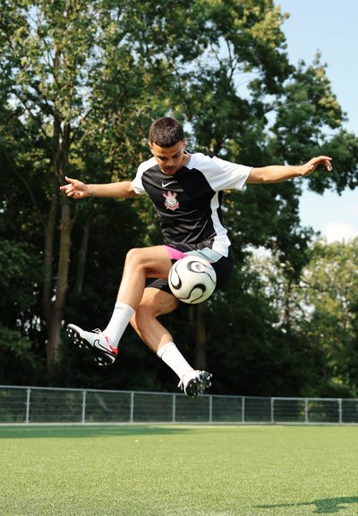 Un joven en un uniforme de fútbol blanco y negro realiza un movimiento hábil con un balón de fútbol blanco y negro, en un campo de césped verde.