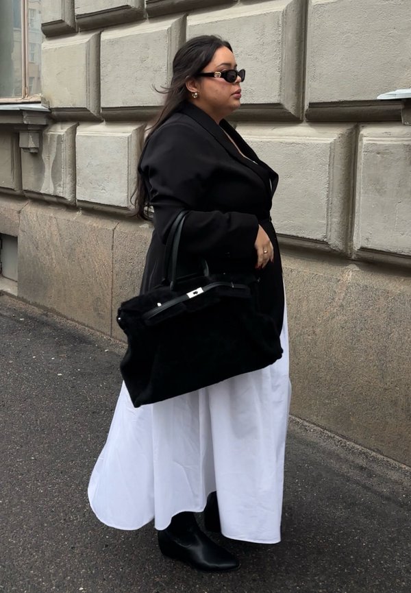 Black oversized blazer worn over a white dress, accessorised with a large black handbag and black ankle boots. Smooth texture, sleek design.