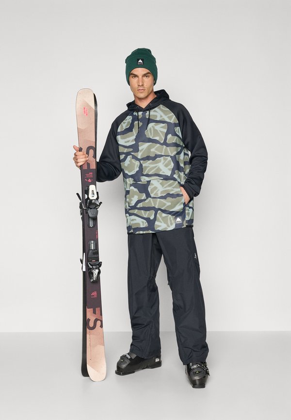 Costumul de schi are un top cu glugă în tonuri de verde și bleumarin cu un model de camuflaj, asortat cu pantaloni waterproof negri; modelul ține schiuri cu legături.