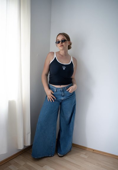 Camiseta de tirantes navy con ribete blanco, que presenta un diseño gráfico, combinada con unos vaqueros de pierna ancha. Las gafas de sol completan el look.