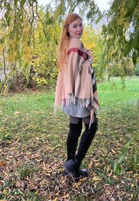 Châle à carreaux beige avec des franges, superposé sur une robe à carreaux noir et blanc, associé à des bottes noires montantes et des collants sombres.