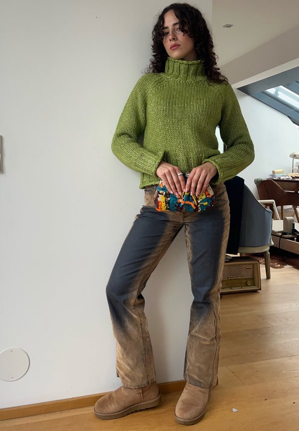 Green knitted jumper with a high collar, paired with dusty blue jeans and tan ankle boots. Holding a colourful patterned clutch bag.