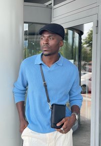 Lyseblå ribbestrikket genser med krage, off-white bukser og en svart crossbody-veske. Sølvsmykker fullfører stilen.