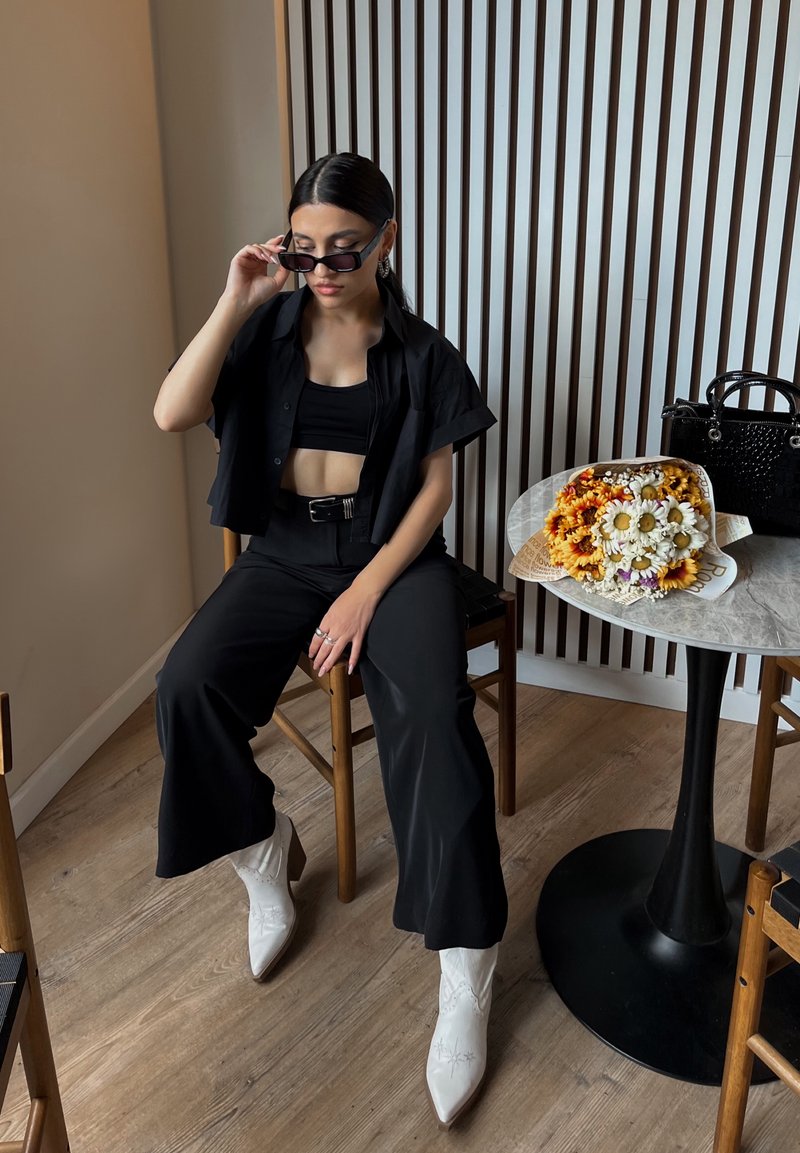 Μαύρο κοντό πουκάμισο, αντίστοιχο κοντό τοπ και παντελόνι σε φαρδιά γραμμή. Λευκές καουμπόικες μπότες με διακοσμητική κλωστή. Λουλουδένια ανθοδέσμη πάνω σε ένα τραπέζι.