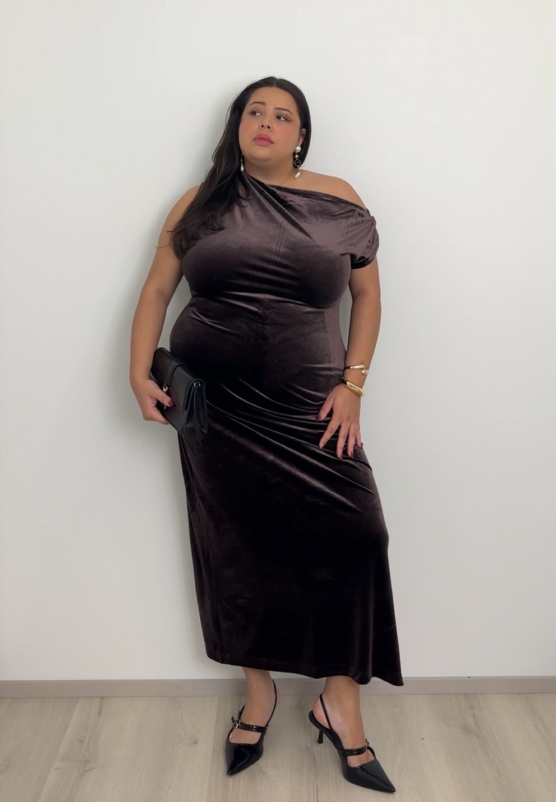 Dark brown, off-shoulder velvet dress with a fitted silhouette, paired with black clutch and pointed toe heels. Smooth texture, mid-length.